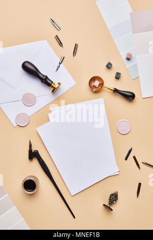 Flat lay of feminine desk workspace with copy space. Calligraphic style, paper and envelope on beige background. Top view with copy space. Stock Photo