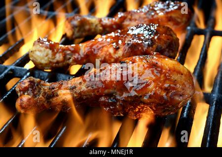 Three chicken legs in BBQ sauce cooking on a flaming grill Stock Photo