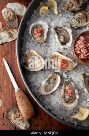 Oysters in shells on a bed of salt with lemon wedges and a Mignonette sauce