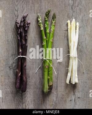 Purple, green and white asparagus stalks on a wooden surface Stock Photo