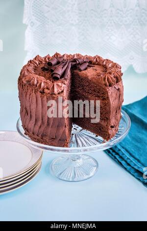 Chocolate layer cake with slice taken out on glass cake stand Stock Photo