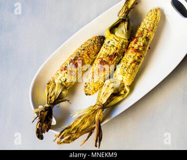 Grilled corn cobs with herbs, cheese and ham Stock Photo