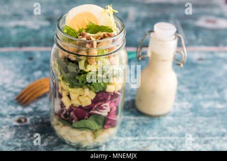 Orzo pasta with lambs lettuce, radicchio, endive, croutons, cheese, walnuts and eggs in a glass jar with dressing and a wooden fork Stock Photo