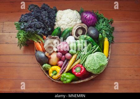 A basket of vegetables on a wooden surface Stock Photo