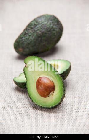 Avocados, whole and halved, on a fabric surface Stock Photo