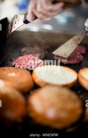 Beefburgers being fried next to toasted buns Stock Photo