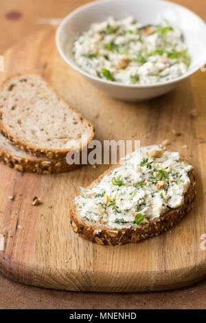 A slice of bread with goats' cheese, spring onion, dandelion greens, thyme and walnuts Stock Photo