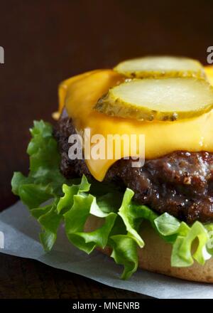 Grilled beef burger on a white bun with curly lettuce, melted cheddar cheese and slices of gherkin Stock Photo