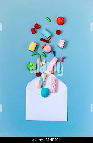 Colourful sweets coming out of an envelope on a light-blue background Stock Photo
