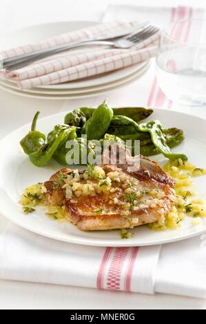 Pork chop with an onion and lemon sauce and grilled chilli peppers Stock Photo