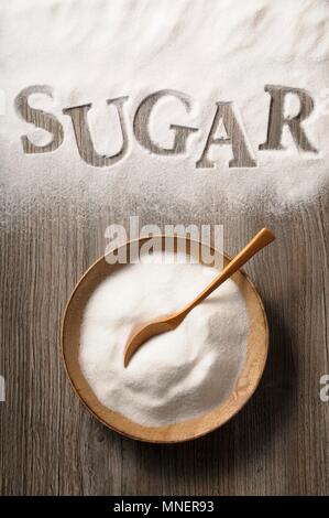 Sugar in a wooden bowl and spilled on a wooden background with the word 'sugar' Stock Photo