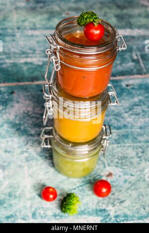 Various colourful soups in glass jars (broccoli soup, tomato soup, pumpkin soup) Stock Photo