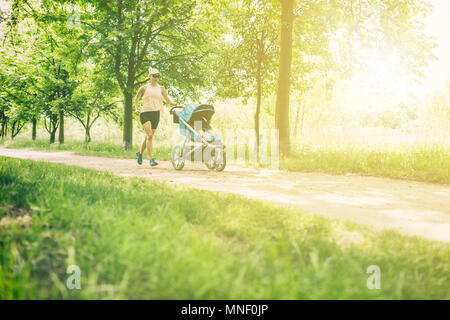 Running woman with baby stroller enjoying summer day in park. Jogging or power walking supermom, active family with baby jogger. Stock Photo