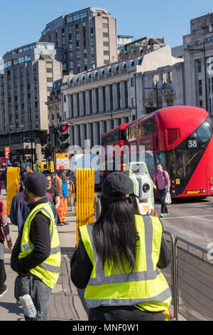 Engineers or civil road workers and site workers taking measurements with a theodolite in central london. High visibility jackets and hard hats london. Stock Photo