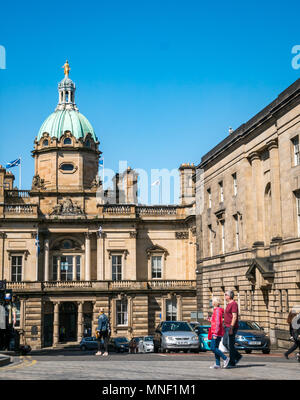 Tourists walking on Royal Mile crossing road past grand building of Bank of Scotland headquarters with copper dome and blue sky Stock Photo