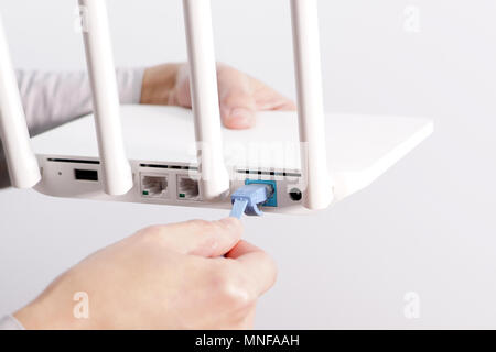 The back view of router showing the lan internet port, and the hand is pluging in the land cable on a white router Stock Photo