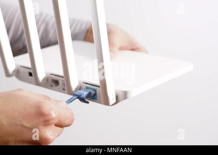 The back view of router showing the lan internet port, and the hand is pluging in the land cable on a white router Stock Photo