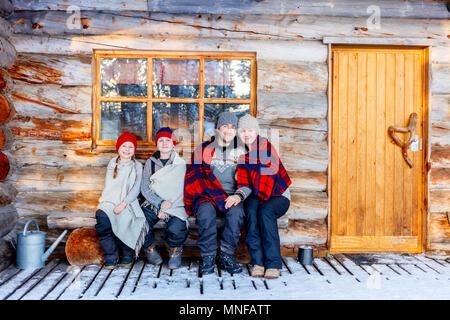 Family with kids outdoors on beautiful winter day in front of log cabin vacation house Stock Photo