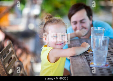Happy little girl at outdoor restaurant or cafe with her father Stock Photo
