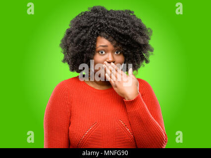 Beautiful african woman covers mouth in shock, looks shy, expressing silence and mistake concepts, scared Stock Photo