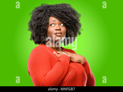 Beautiful african woman having charming smile holding hands on heart wanting to show love and sympathy Stock Photo