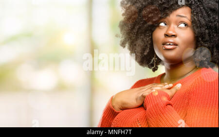 Beautiful african woman having charming smile holding hands on heart wanting to show love and sympathy, outdoor Stock Photo