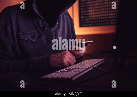 Computer hacker using smartphone device in dark interior, low key with selective focus Stock Photo