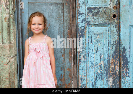 Portrait of adorable little girl outdoors on a street against old door Stock Photo