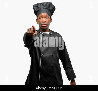 Young black cook wearing chef hat pointing to the front with finger