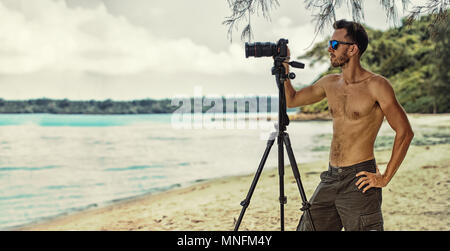 man freelancer working outdoor, holding in hands digital camera and doing photo and video shoot on the background of scenery nature Stock Photo