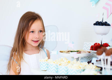 Adorable little fairy girl on a birthday party in front of dessert table