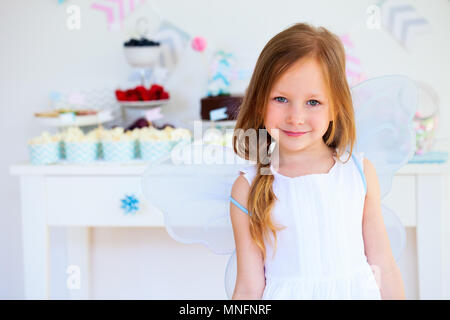 Adorable little fairy girl with wings on a birthday party near dessert table Stock Photo