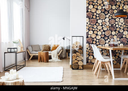 Wooden log texture wallpaper in cozy dining space of white open plan apartment with sofa, rug and tree stump accessories Stock Photo