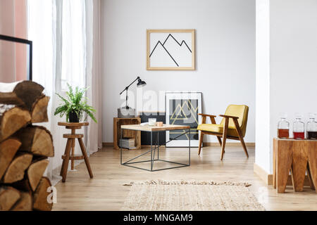 Modern designed interior of cozy white living room with coffee table, armchair, posters and firewood Stock Photo