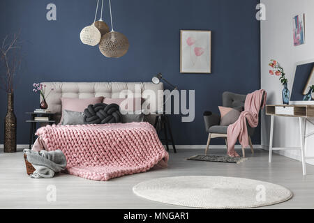 Dark grey comfy armchair with cushion and pink blanket in the corner of the room Stock Photo