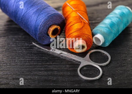 colored threads and scissors on a black wooden background Stock Photo