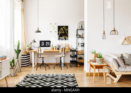 Contemporary room in scandinavian style with office interior with desk, poster, retro chairs and cactus and open living room with sofa and wooden furn Stock Photo