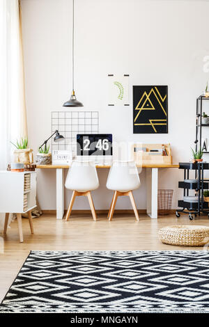Stylish patterned rug, wicker pouf and natural accessories in modern apartment with white wall and scandinavian design of desk workspace Stock Photo