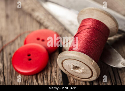 red thread with buttons and scissors, wooden background Stock Photo