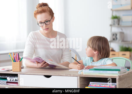 Young boy and teacher sitting in classroom during language lesson. Preschool education concept Stock Photo