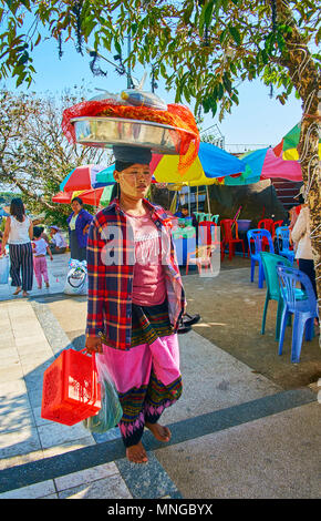 KYAIKTIYO, MYANMAR - FEBRUARY 16, 2018:   The young street vendor with thanaka decoration on the face is carrying large bown with Burmese snacks of se Stock Photo