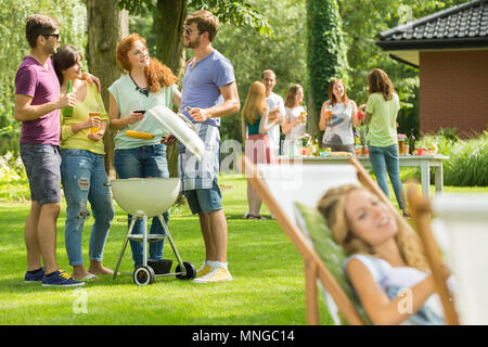 Young man grilling food while talking with friends Stock Photo