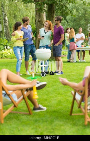 Friends standing beside barbecue grill, people resting on deckchairs Stock Photo