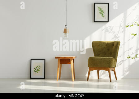White room with green armchair, wooden table and botanical posters Stock Photo