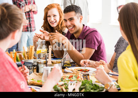 Smiling man in violet shirt eats slow food with happy vegetarians in vege restaurant Stock Photo