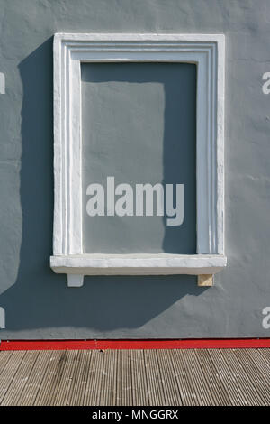 Gray plastered wall and blind imitation window with a white frame. Real sunny day outdoor shot Stock Photo