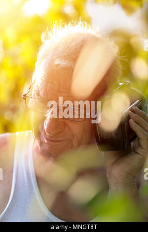 The old man standing outdoor and listen to a portable radio Stock Photo