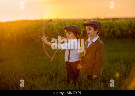 Portrait of children playing with bow and arrows, archery shoots a bow at the target on sunset Stock Photo