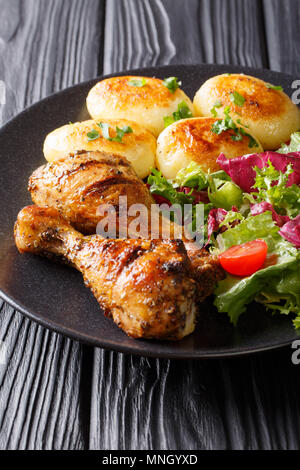 Delicious food: grilled chicken drumsticks with new potatoes and fresh salad closeup on a plate on the table. vertical Stock Photo