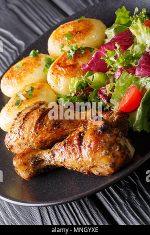 Grilled chicken drumsticks are served with potatoes and fresh salad close-up on the table. vertical Stock Photo